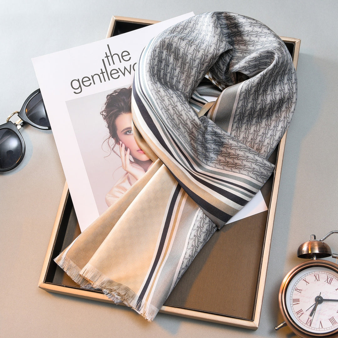 A neatly folded Luxurious Men's Silk Twill Scarf - Grey Khaki by SusanSilk with a patterned design lies on a magazine cover featuring a woman. Nearby are sunglasses and an analog clock.