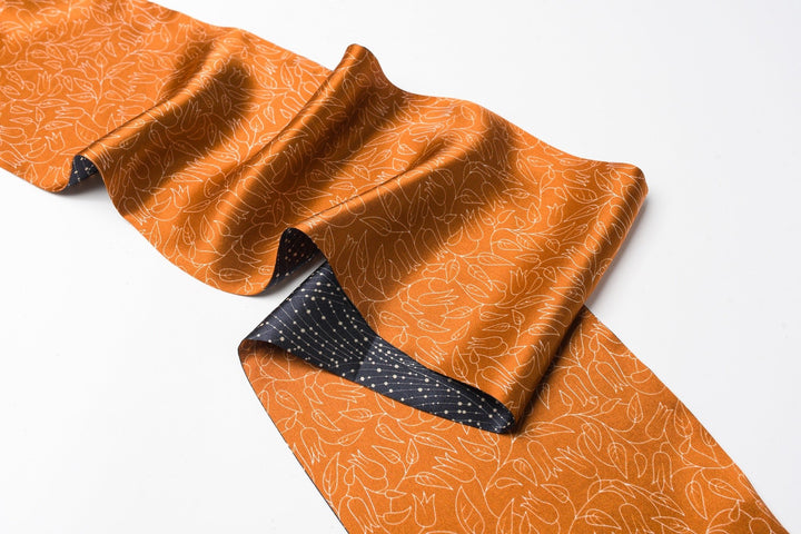 The Orange Flower Sprigs Silk Long Fluttering Belt from SusanSilk features an orange and black patterned fabric with a floral design on a white background.