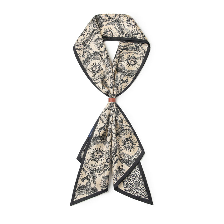 The 16 Momme Affordable Luxury Silk Twill Long Silk Scarf-Gerbera by SusanSilk is a long, narrow silk scarf adorned with a black and white celestial pattern featuring stars and suns, tied in a simple knot with a red accent in the center.