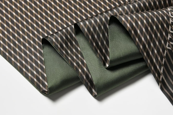 Close-up of the Luxurious Men's Silk Twill Scarf in Green by SusanSilk, featuring a folded green silk fabric with a geometric pattern in brown, black, and white on top. The pattern consists of diagonal lines forming a diamond grid.