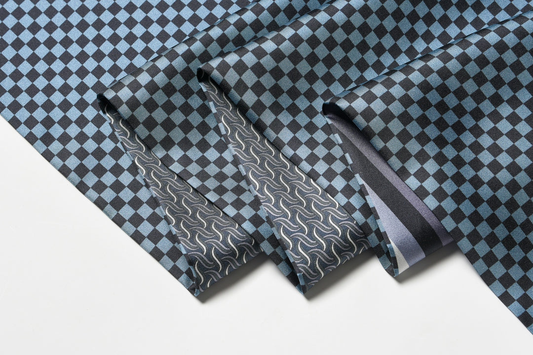 Two patterned silk scarves are laid out flat. One displays a brown and white checkered pattern, while the other is the Luxurious Men's Silk Twill Scarf - Grey Khaki from SusanSilk, featuring a grey and white herringbone design with striped borders.