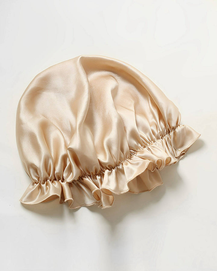 A Flounced Silk Bonnet For Sleeping by SusanSilk, featuring ruffled edges and crafted from luxurious beige silk, laid flat on a light surface.