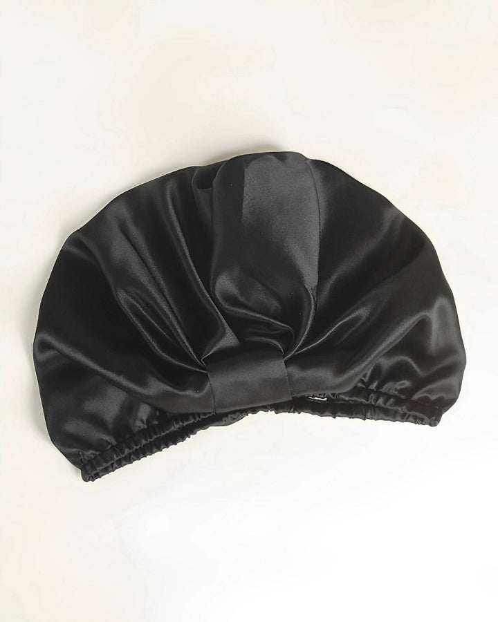 An Elegant Pleated Silk Bonnet For Sleeping from SusanSilk, in black with an elastic band, lies on a white surface.