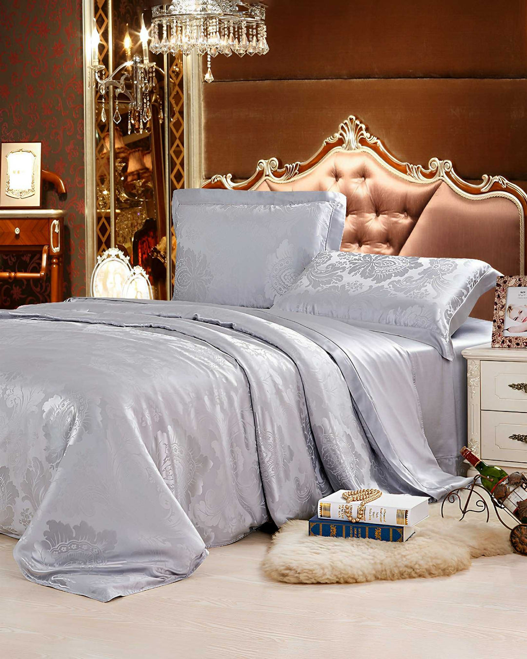 A luxurious bedroom features an ornate tufted headboard, chandelier, and a neatly made bed adorned with the 19 Momme Jacquard Silk Bedding Set by SusanSilk. A side table holds a lamp, and books rest on a fur rug nearby.