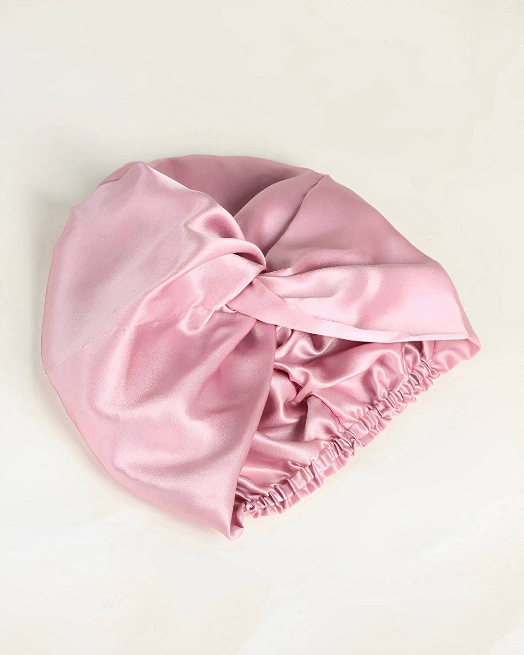 A luxurious pink satin Luxury Turban Silk Sleep Cap with an elastic band and a twisted knot design, crafted from high-quality SusanSilk, set against a light background.