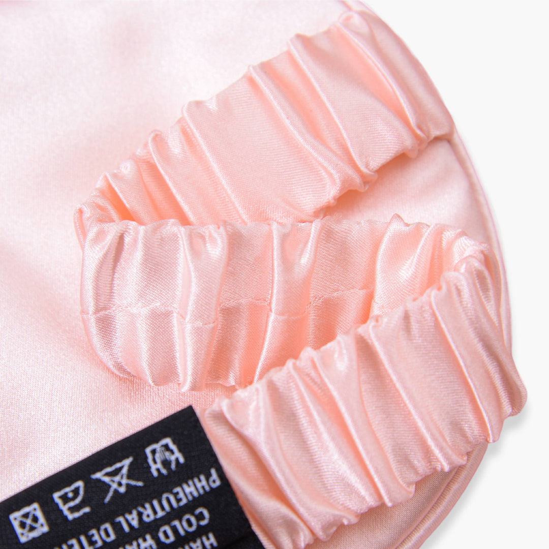 Close-up of the Elegant Silk Eye Mask - Pink Canyon by SusanSilk, showcasing its pink satin fabric with elastic bands and a tag displaying silk washing instructions.