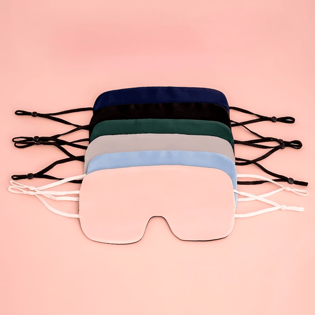 A set of five luxurious SusanSilk Oversized Silk Eye Masks in different colors (black, navy blue, dark green, gray, and light blue) arranged neatly on a peach background.