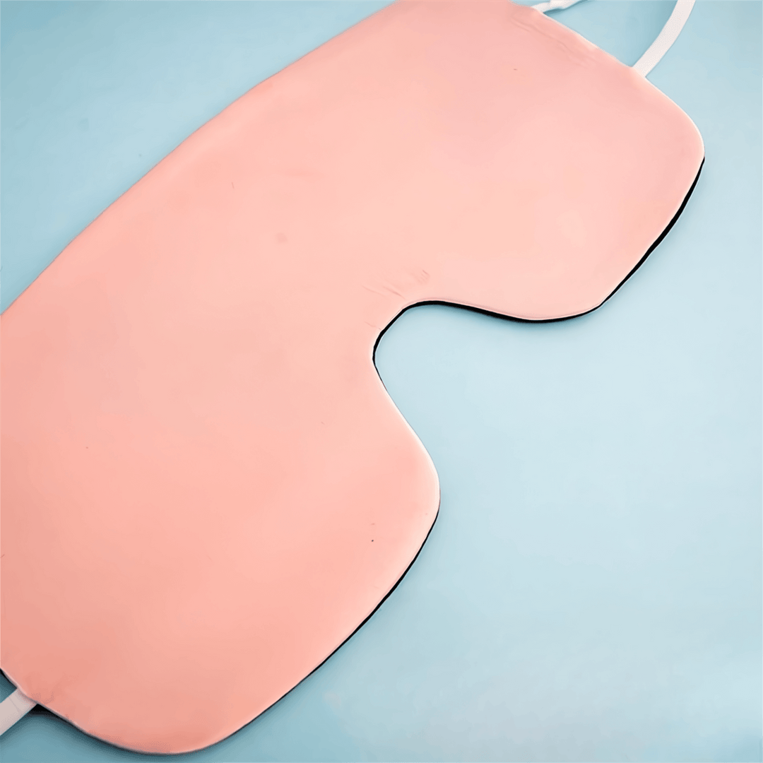 The Oversized Silk Eye Mask by SusanSilk, featuring pink silk and white elastic bands, is placed on a light blue surface.