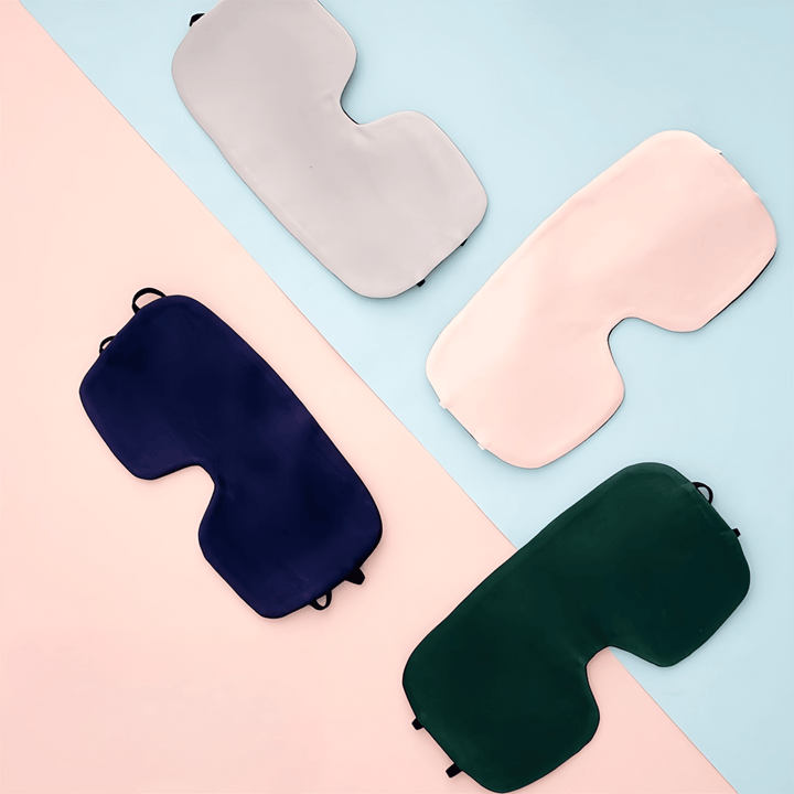 Image of four SusanSilk Oversized Silk Eye Masks arranged on a diagonal split background of light pink and light blue. The masks come in grey, light pink, navy blue, and dark green colors.