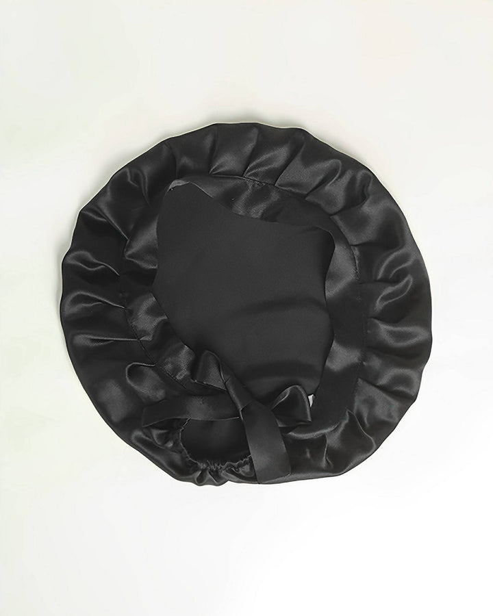 A black Chic Silk Bonnet For Sleeping with Ribbons by SusanSilk, featuring a ruffled edge, laid flat on a white background, showcases the luxurious feel of silk.