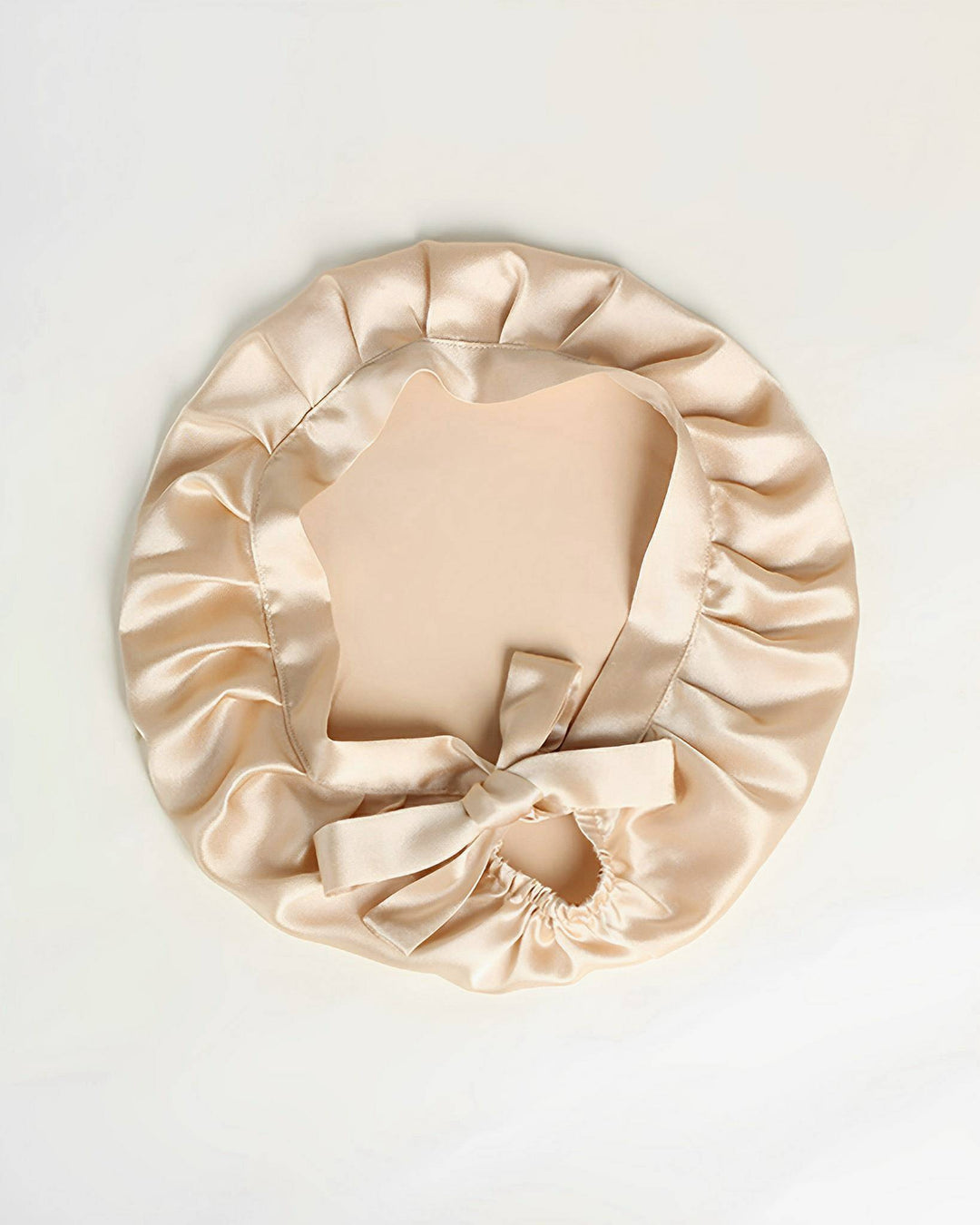 A Chic Silk Bonnet for Sleeping with Ribbons by SusanSilk, in beige satin featuring a ruffled edge and a bow at the front, displayed on a white background.