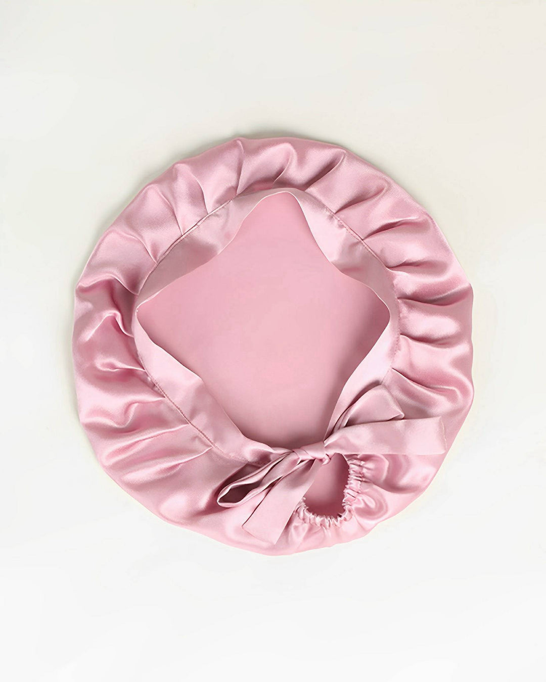 A Chic Silk Bonnet For Sleeping with Ribbons by SusanSilk, featuring ruffled edges and a ribbon bow, rests on a white background.