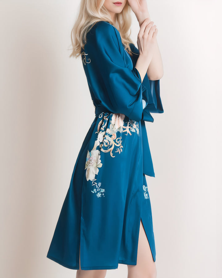 A person with long blonde hair wearing the SusanSilk Peony Floral Short Silk Kimono poses gracefully against a plain background, their attire exuding luxurious elegance.