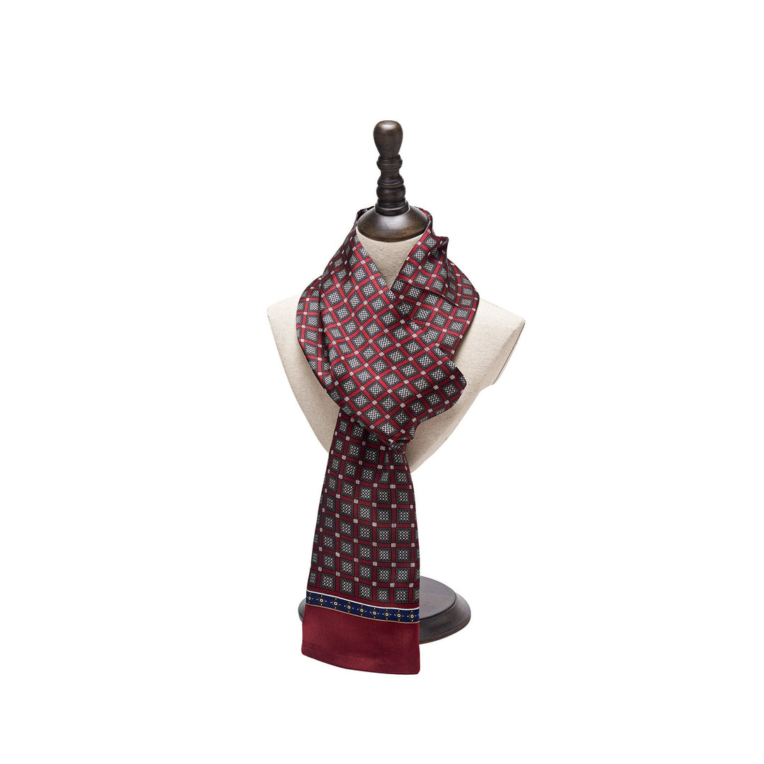 A Journey Grid Series Long Silk Scarf from SusanSilk, featuring a sophisticated red and blue pattern, is elegantly draped on a cream-colored mannequin bust with a dark wooden stand.