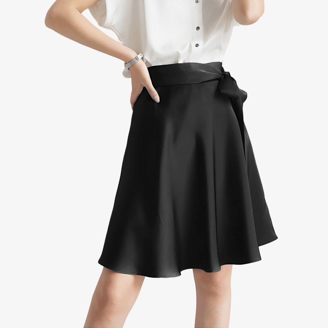 Person wearing a white short-sleeve blouse and a SusanSilk Bow Tie Knee Length Silk Skirt in black, with one hand on their hip.