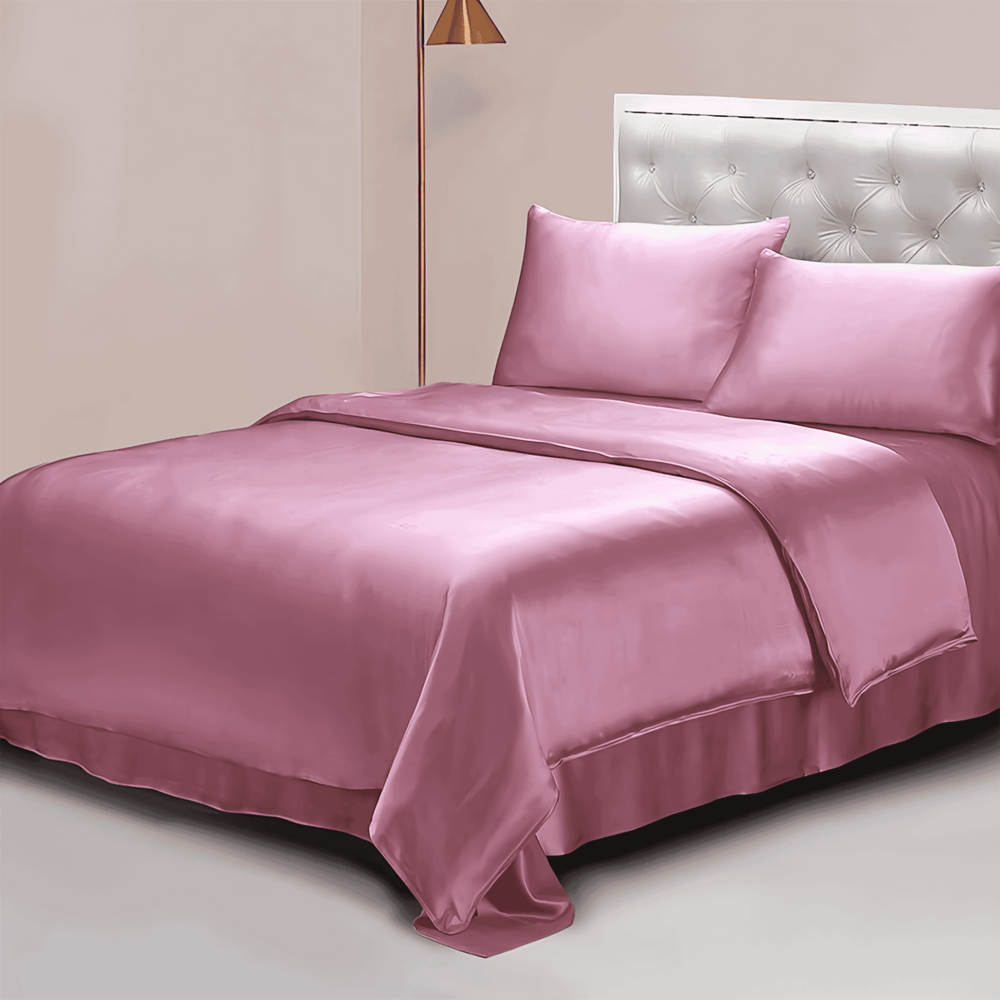 A neatly made bed with a tufted headboard, adorned with the SusanSilk 22 Momme Luxury Silk Bedding Set - 4Pcs in pink, including sheets, pillowcases, and a comforter. An angled floor lamp stands beside the bed on the left.