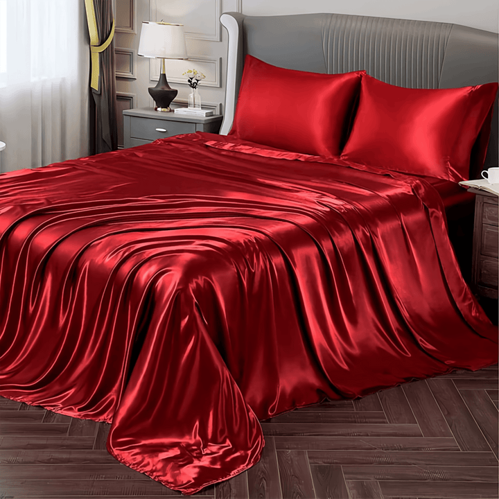 A modern bedroom featuring the SusanSilk 22 Momme Luxury Silk Bedding Set - 4Pcs, complete with elegant red satin sheets and matching pillowcases. The room is complemented by a lamp and nightstand, with natural light streaming through curtains to accentuate the opulent feel of the silk bedding.