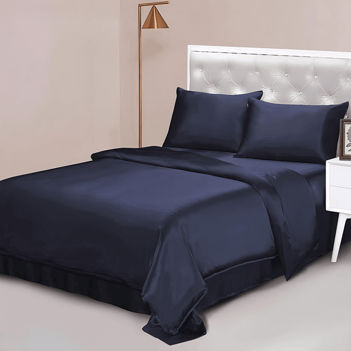 A modern bedroom featuring a bed adorned with the 22 Momme Luxury Silk Bedding Set in navy blue from SusanSilk, including two pillows, a tufted white headboard, and accompanied by a white nightstand with a frame and a floor lamp.