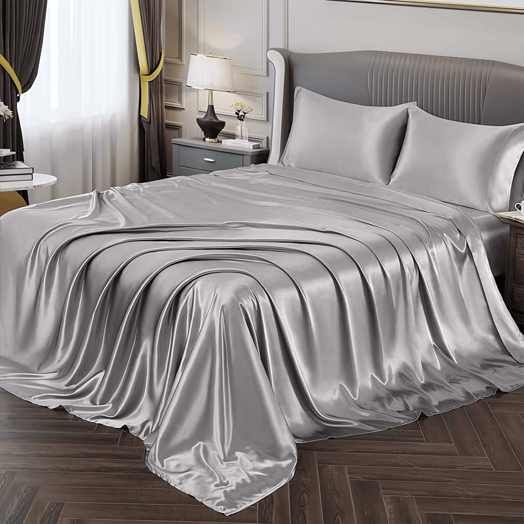 A neatly made bed adorned with the 22 Momme Luxury Silk Bedding Set - 4Pcs by SusanSilk, positioned in a well-lit bedroom with grey walls, a bedside table, and a lamp.