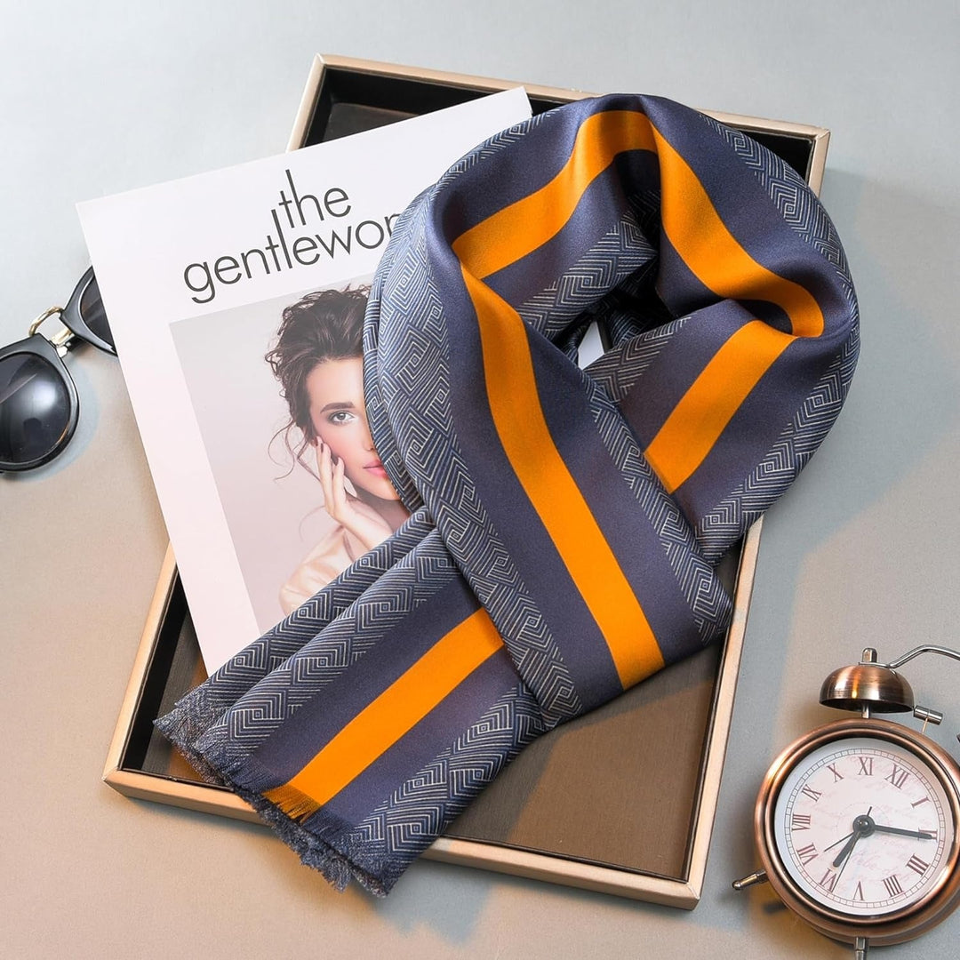 A blue and yellow silk twill scarf from SusanSilk is neatly arranged on top of a magazine within a wooden tray, accompanied by a pair of sunglasses and an alarm clock.