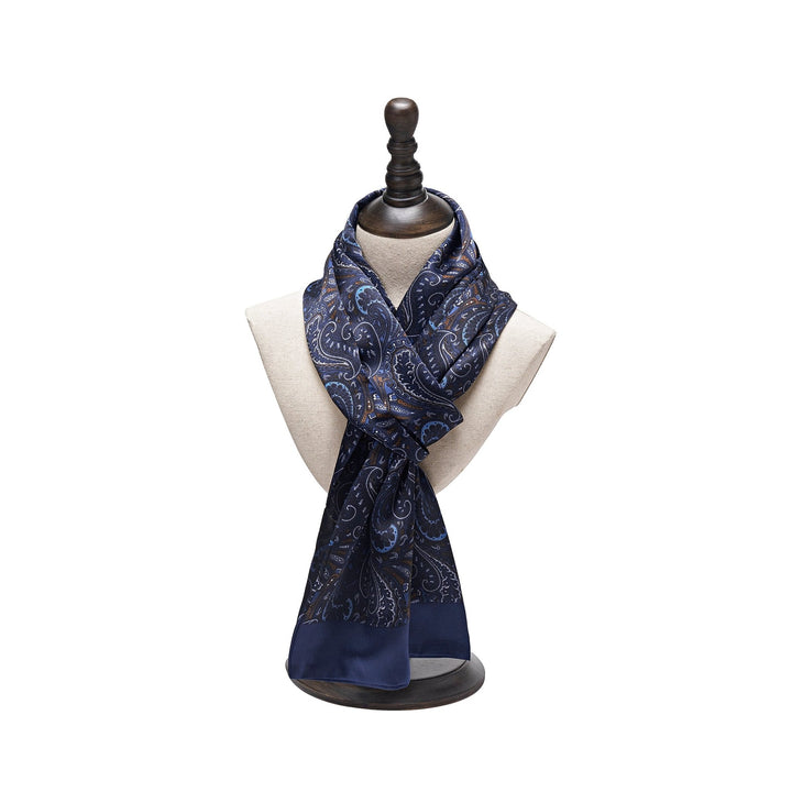 A Paisley Series Long Silk Scarf in a luxurious navy blue pattern is draped around a white mannequin bust on a wooden stand, showcasing the elegance of SusanSilk.