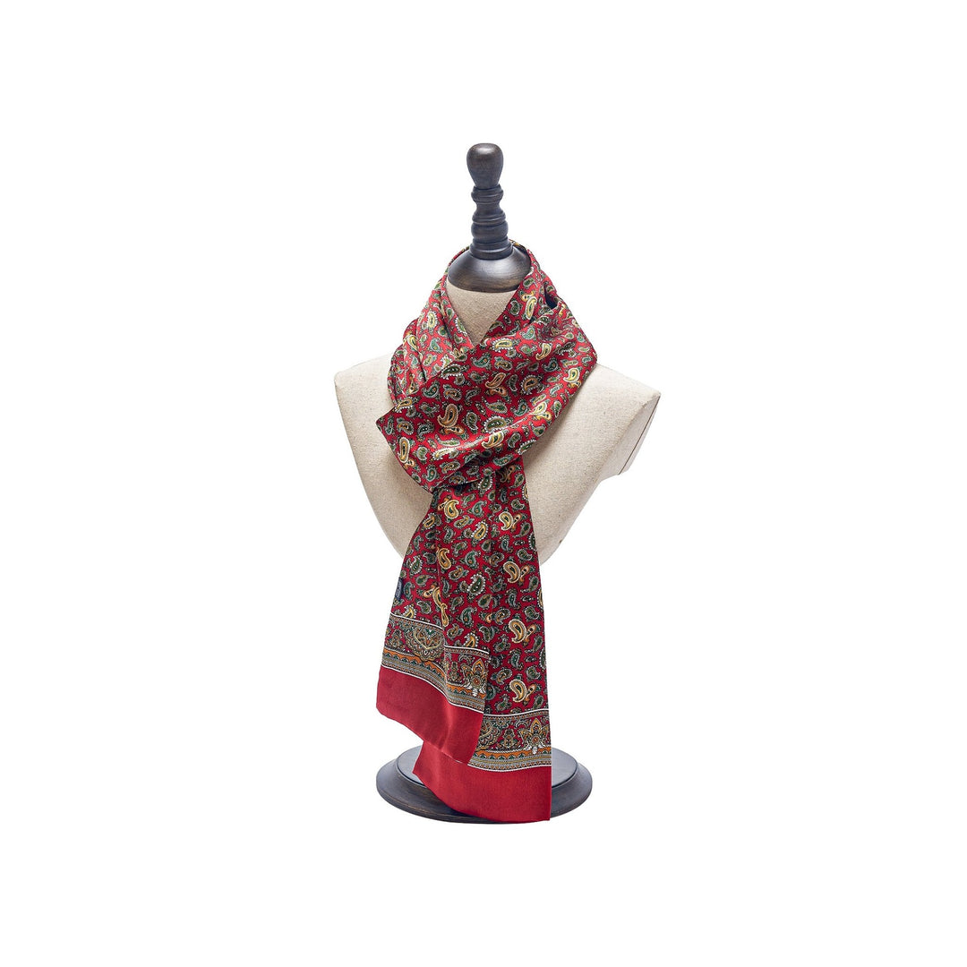 A luxurious silk scarf from SusanSilk's Paisley Series, featuring intricate designs and borders in a vibrant red pattern, is displayed on a white mannequin with a dark base and stand.