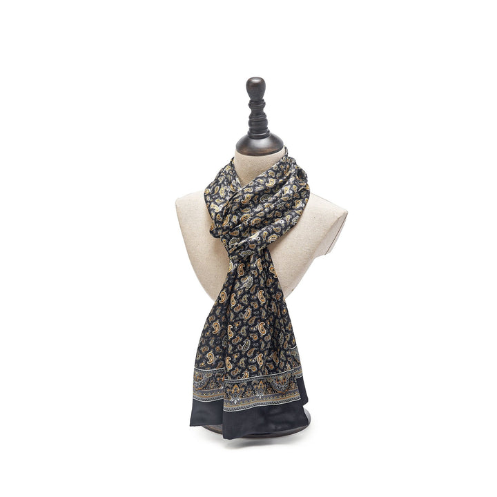 A SusanSilk mannequin bust showcasing the Paisley Series Long Silk Scarf, featuring an opulent black paisley pattern with elaborate gold and blue designs, elegantly draped around the neck against a white background.