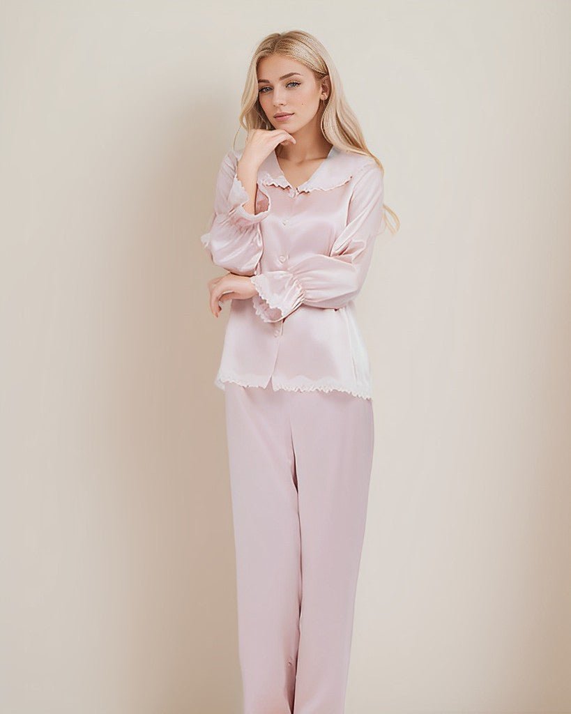 A woman with long blonde hair is posing thoughtfully in light pink 22 Momme Lace Silk Pajamas Set by SusanSilk against a plain background.