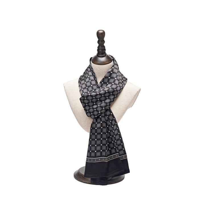 A SusanSilk Journey Grid Series Long Silk Scarf, featuring a black and white pattern, draped around a beige mannequin bust on a wooden stand.