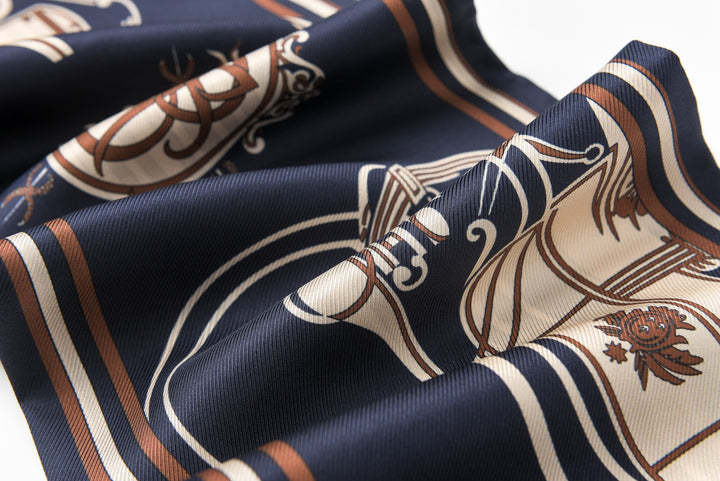 Close-up of the 16 Momme Affordable Luxury Silk Twill Long Silk Scarf-Blue Striped Wagon by SusanSilk, showcasing its dark blue silk fabric with intricate beige and brown patterns, along with visible folds and creases.