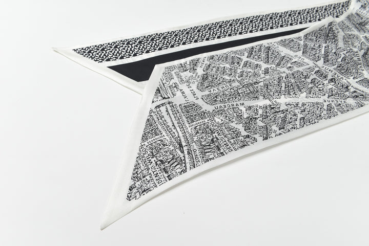 Close-up of the 16 Momme Affordable Luxury Silk Twill Long Silk Scarf in Black & White City by SusanSilk, showcasing an intricate city map design printed on the triangular fabric piece, layered atop another fabric featuring a black and white dotted pattern.