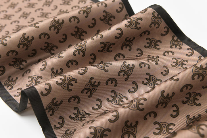 A close-up view of the SusanSilk 16 Momme Affordable Luxury Silk Twill Long Silk Scarf-Classic Arc de Triomphe, showcasing its light brown silk fabric with a repeating black pattern and a solid black edge.