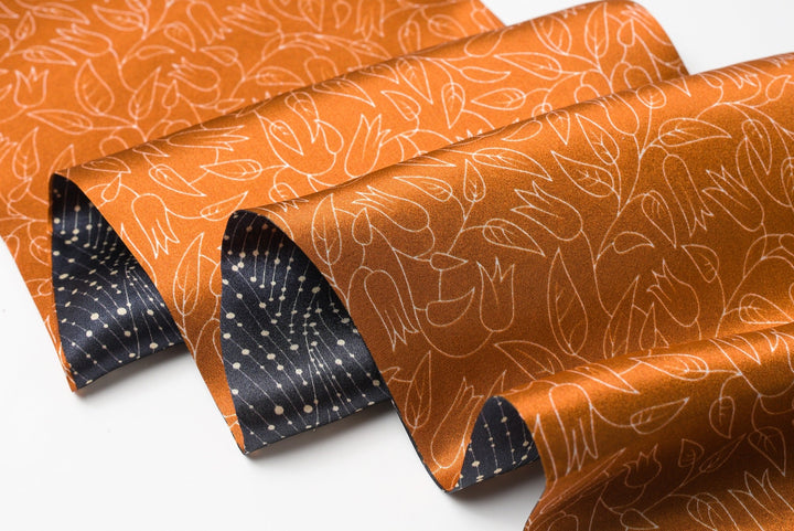 Close-up of the SusanSilk Orange Flower Sprigs Silk Long Fluttering Belt, revealing its intricate white floral pattern on the vibrant orange fabric, partially covering a black silk piece adorned with white polka dots.