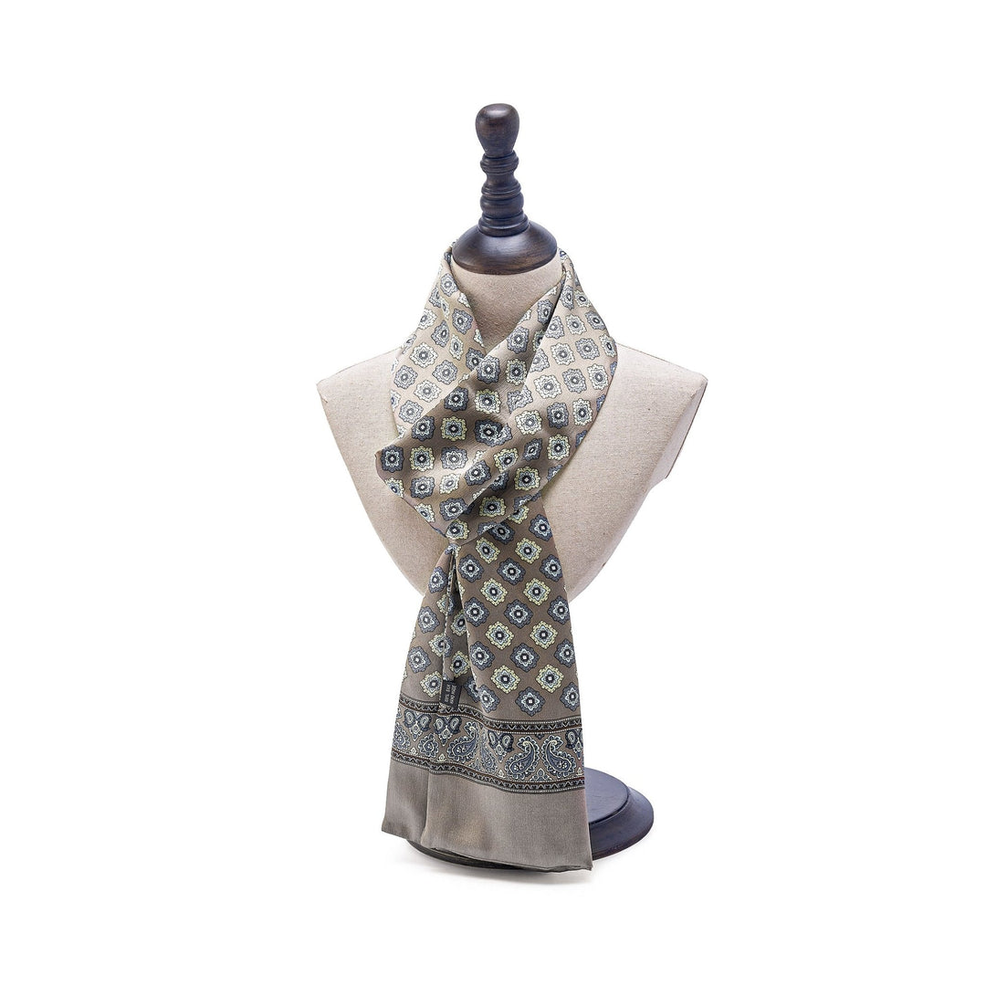 A Geometric Pattern Long Silk Scarf from SusanSilk, featuring beige and blue designs, is draped around a beige mannequin bust on a black stand.