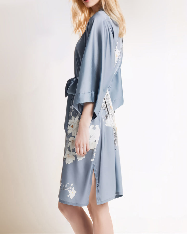 A person with long blonde hair is wearing a White Lilies Short Silk Kimono by SusanSilk, featuring floral patterns.