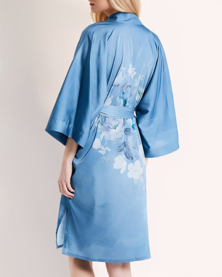 A person with long hair is wearing a Blue Floral Short Silk Kimono from SusanSilk, shown from the back, the delicate fabric shimmering like moonlight.