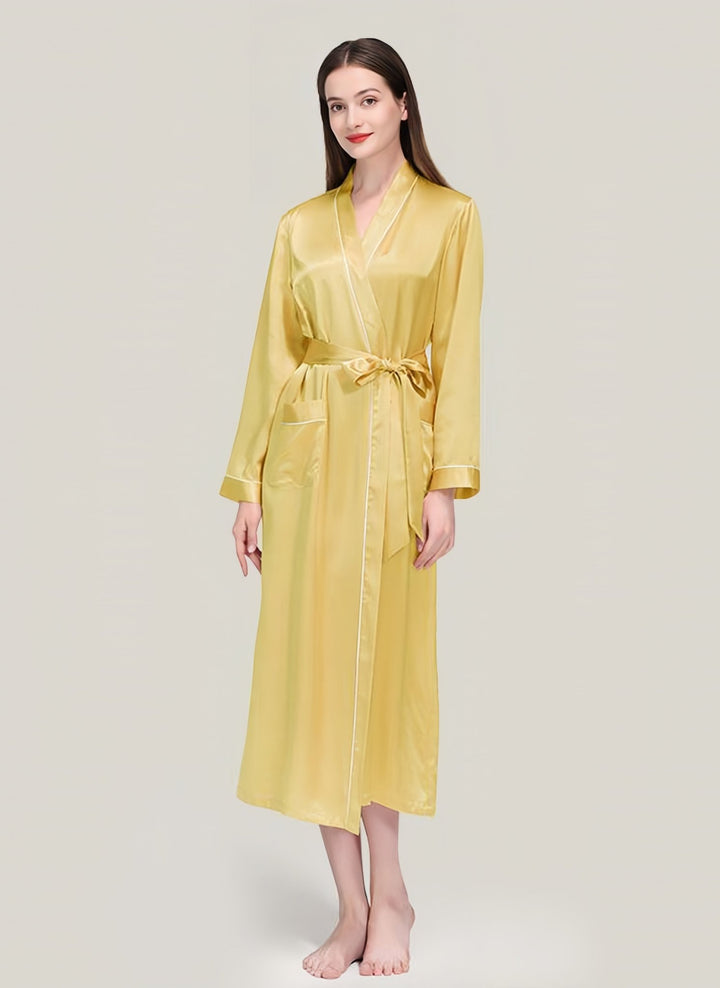 A person stands barefoot wearing the luxurious 22 Momme Contrast Piping Long Silk Robe for women from SusanSilk, featuring a long yellow satin finish with a belt.