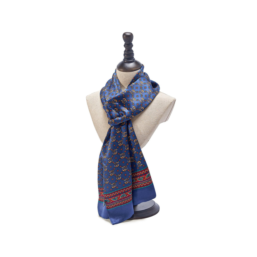 A "Paisley Series Long Silk Scarf" by SusanSilk, featuring a blue pattern with red and beige accents, elegantly draped on a beige mannequin bust with a black stand.