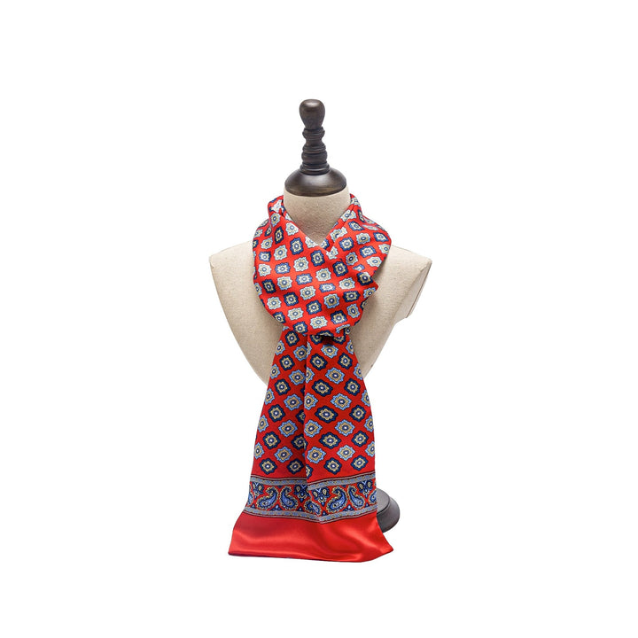 The Geometric Pattern Long Silk Scarf by SusanSilk, featuring luxurious red silk adorned with blue and white designs, is elegantly displayed on a beige mannequin bust with a dark brown stand.