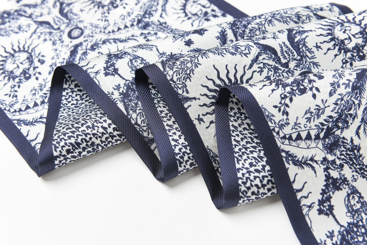 A close-up of the 16 Momme Affordable Luxury Silk Twill Long Silk Scarf-Gerbera by SusanSilk, showcasing its intricate blue and white pattern featuring various detailed motifs.