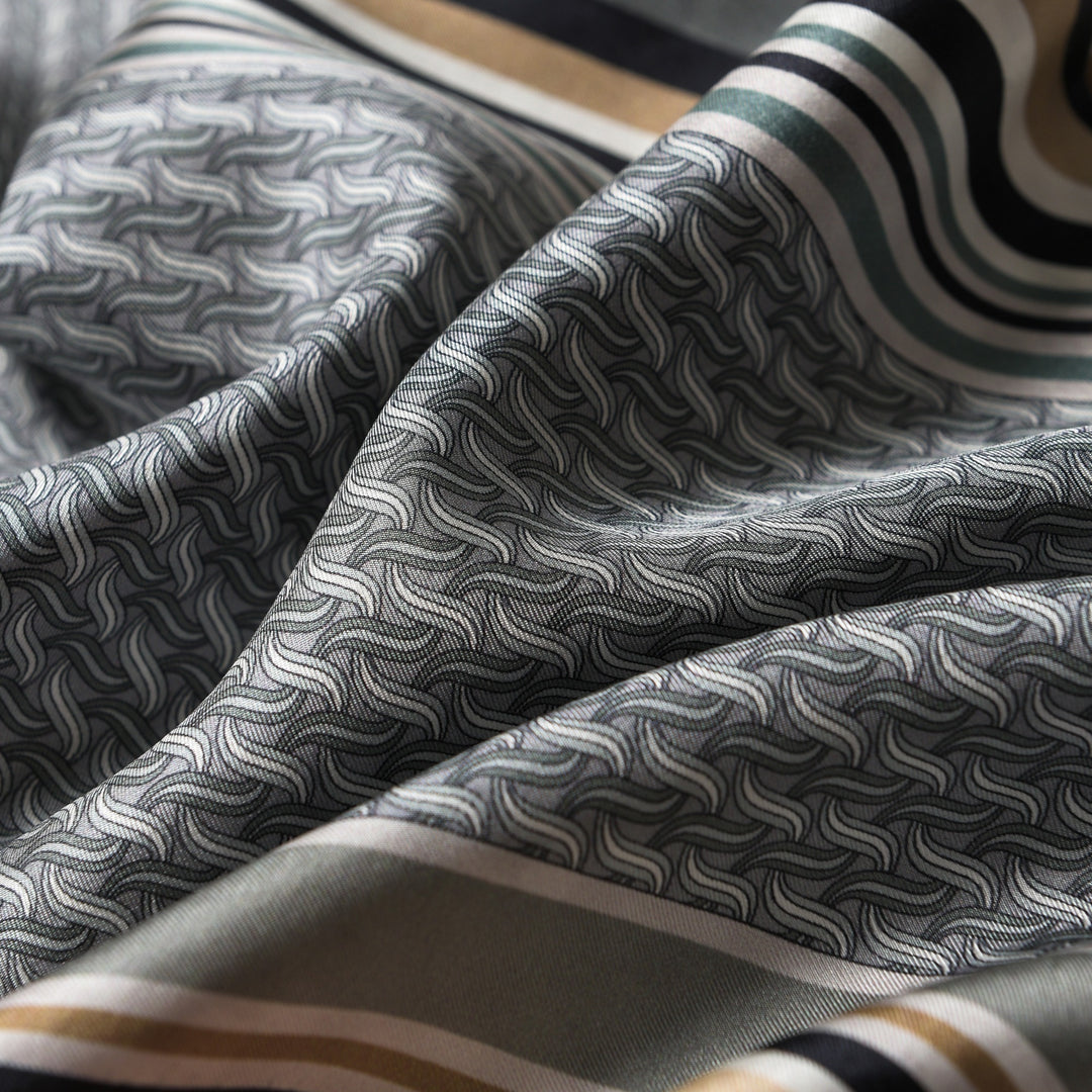 Close-up of a folded Luxurious Men's Silk Twill Scarf in Grey Khaki by SusanSilk, showcasing a wavy, intricate pattern in shades of gray, green, and brown with striped edges.