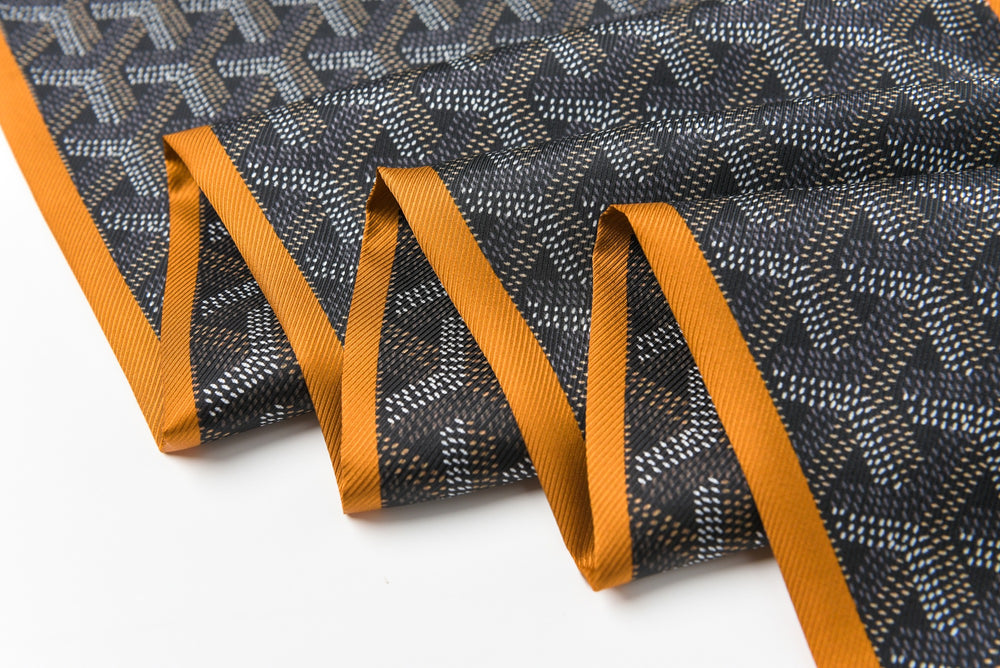 Close-up of the SusanSilk 16 Momme Affordable Luxury Silk Twill Long Silk Scarf-Cubic Orange, showcasing its black and white pattern with an orange border, gracefully folded in pleats.