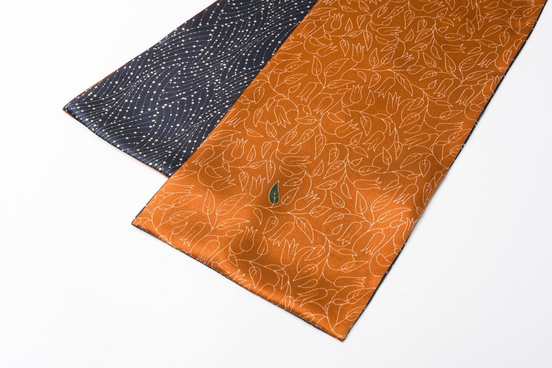 A black silk necktie with a gold dotted pattern lies next to the Orange Flower Sprigs Silk Long Fluttering Belt by SusanSilk, both on a plain white background.