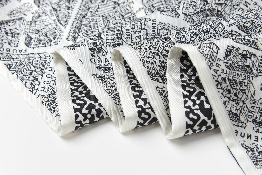 A close-up of folded SusanSilk’s 16 Momme Affordable Luxury Silk Twill Long Scarf in black and white, showcasing an intricate city map pattern.