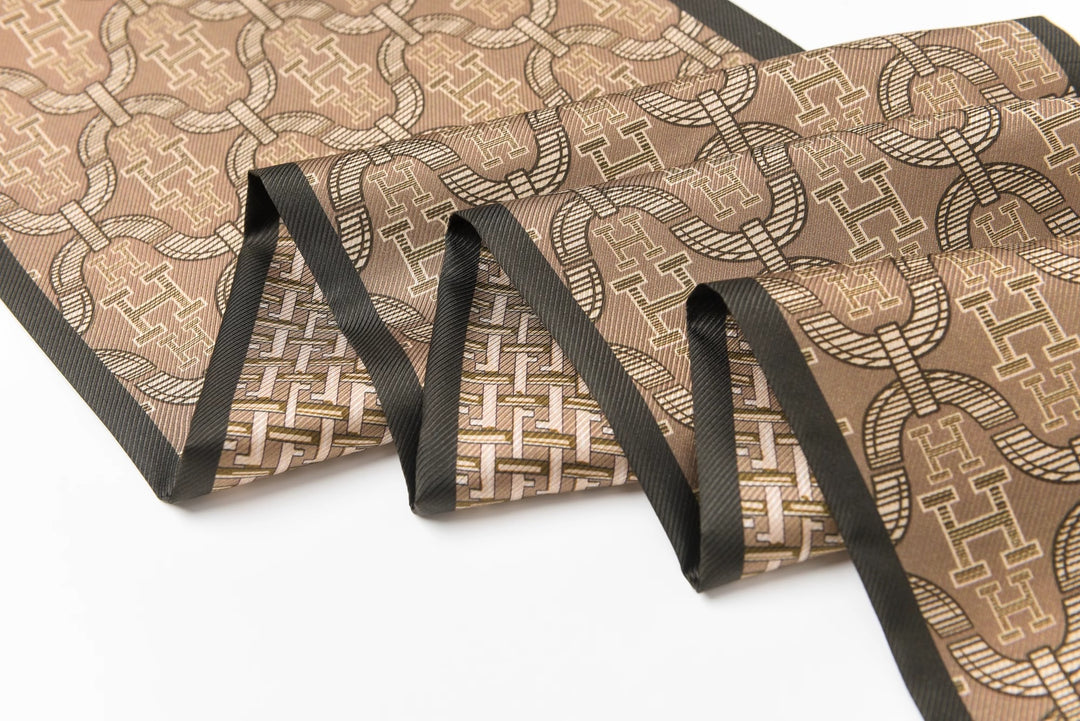 A 16 Momme Affordable Luxury Silk Twill Long Silk Scarf-Classic H Style from SusanSilk, featuring a folded fabric with a brown geometric pattern of interlocking circles and rectangular motifs, bordered by dark edges.