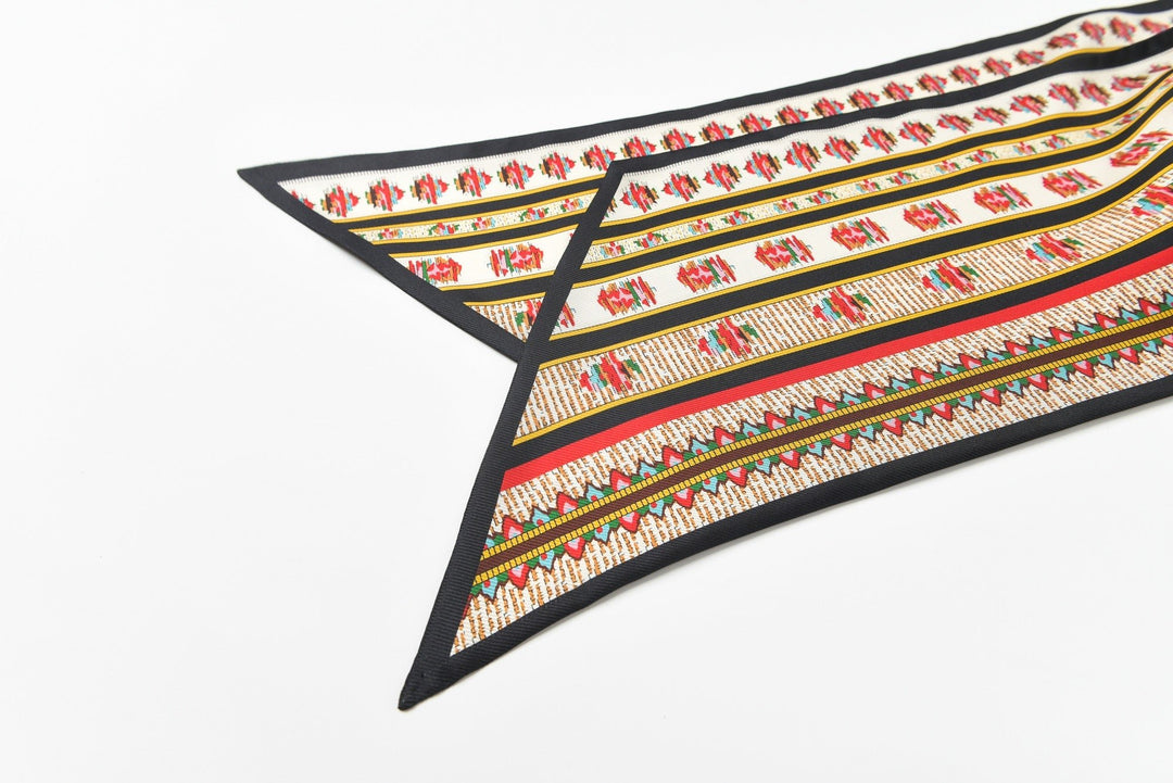 A fabric with colorful, intricate patterns featuring rows of geometric designs and small floral motifs accented by black borders. Made from luxurious SusanSilk's 16 Momme Affordable Luxury Silk Twill Long Silk Scarf-Crushed Flower, the material is laid flat showing its triangular ends.