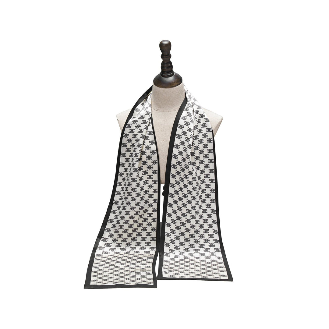 The SusanSilk Arc De Triomphe Narrow Long Silk Scarf, featuring a black and white houndstooth pattern with a black border, is elegantly displayed on a mannequin bust, gracefully hanging down on both sides.