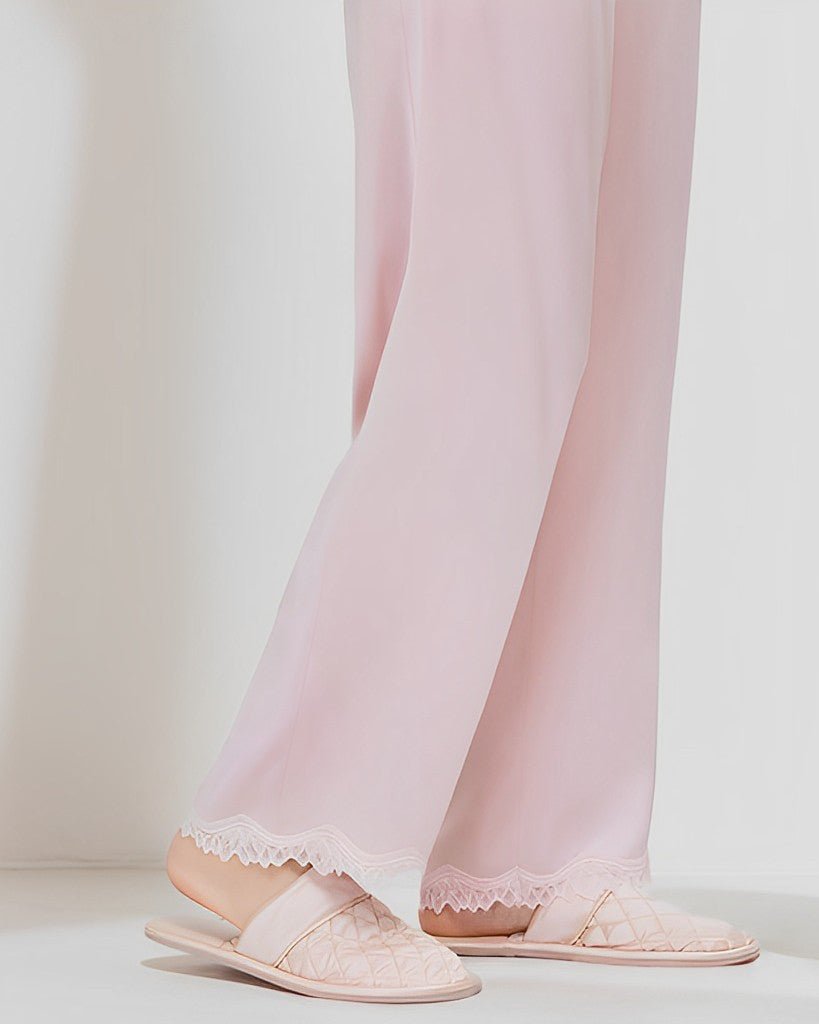 A person wearing pale pink 22 Momme Lace Silk Pajamas Set and matching quilted slippers from SusanSilk. Only the lower half of the body is visible.