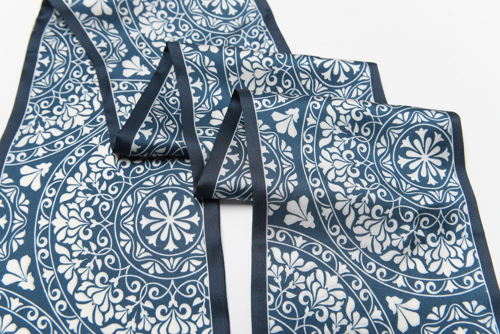 A folded piece of the Blue And White Silk Long Fluttering Belt by SusanSilk, featuring an intricate blue and white floral and geometric pattern on a white background.