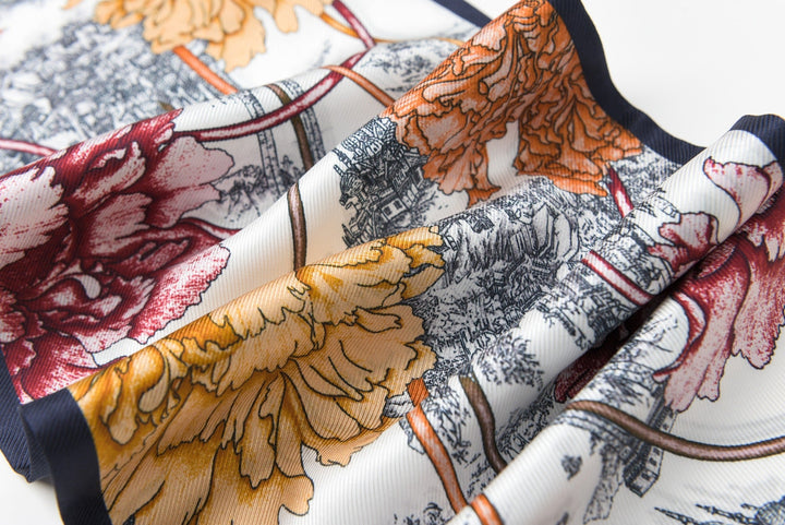 Close-up of SusanSilk's 16 Momme Affordable Luxury Silk Twill Long Silk Scarf-Peony Mirage, showcasing a luxuriant silk fabric adorned with a colorful floral and scenic pattern in vibrant hues of red, yellow, and orange against a white background.